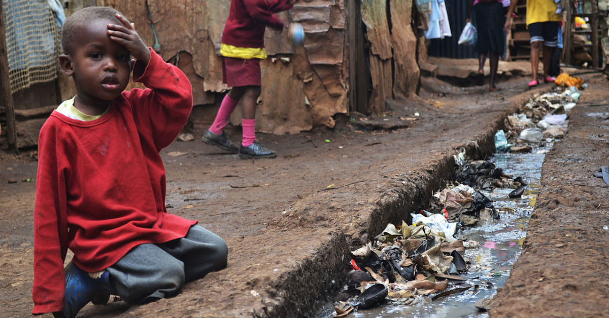 A young boy sits over an open sewer in Kibera, Nairobi