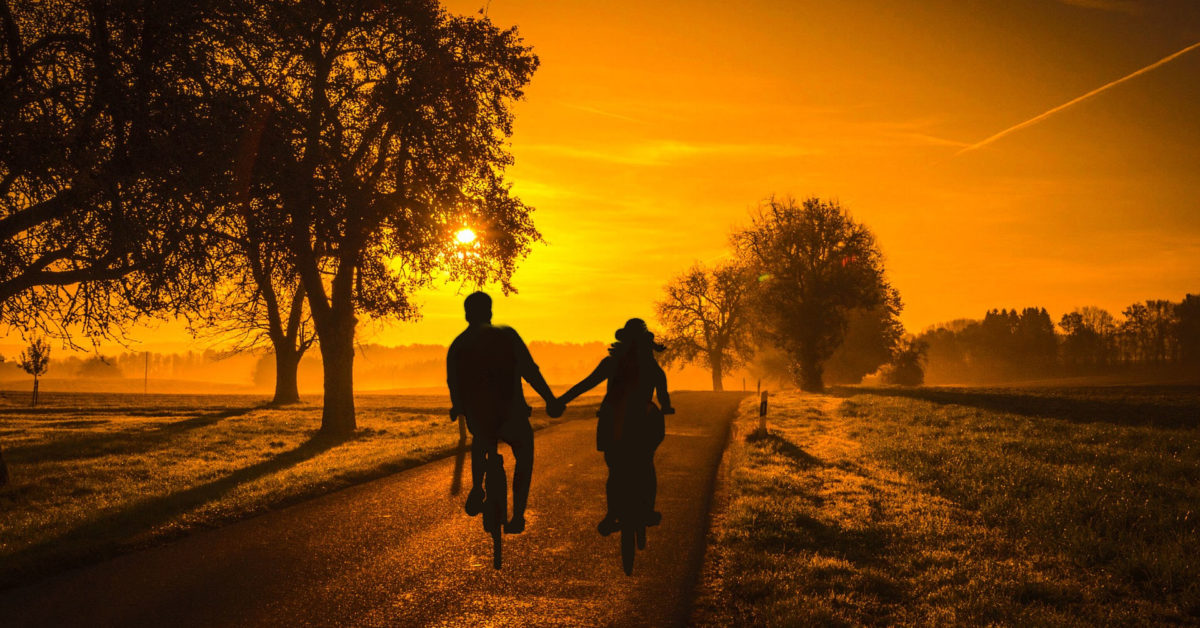 Two people riding bicycles into the sunset in the countryside