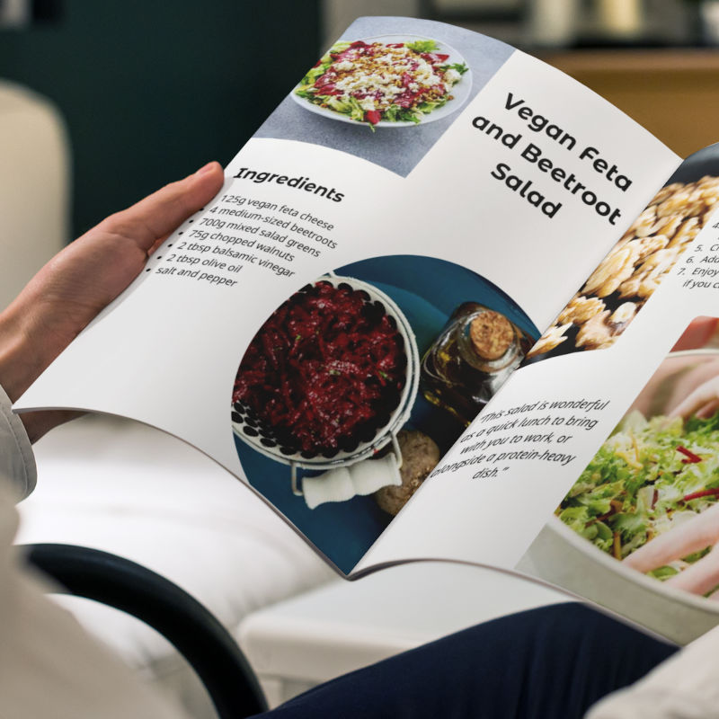 A man holding an open copy of the vegan cookbook in his living room